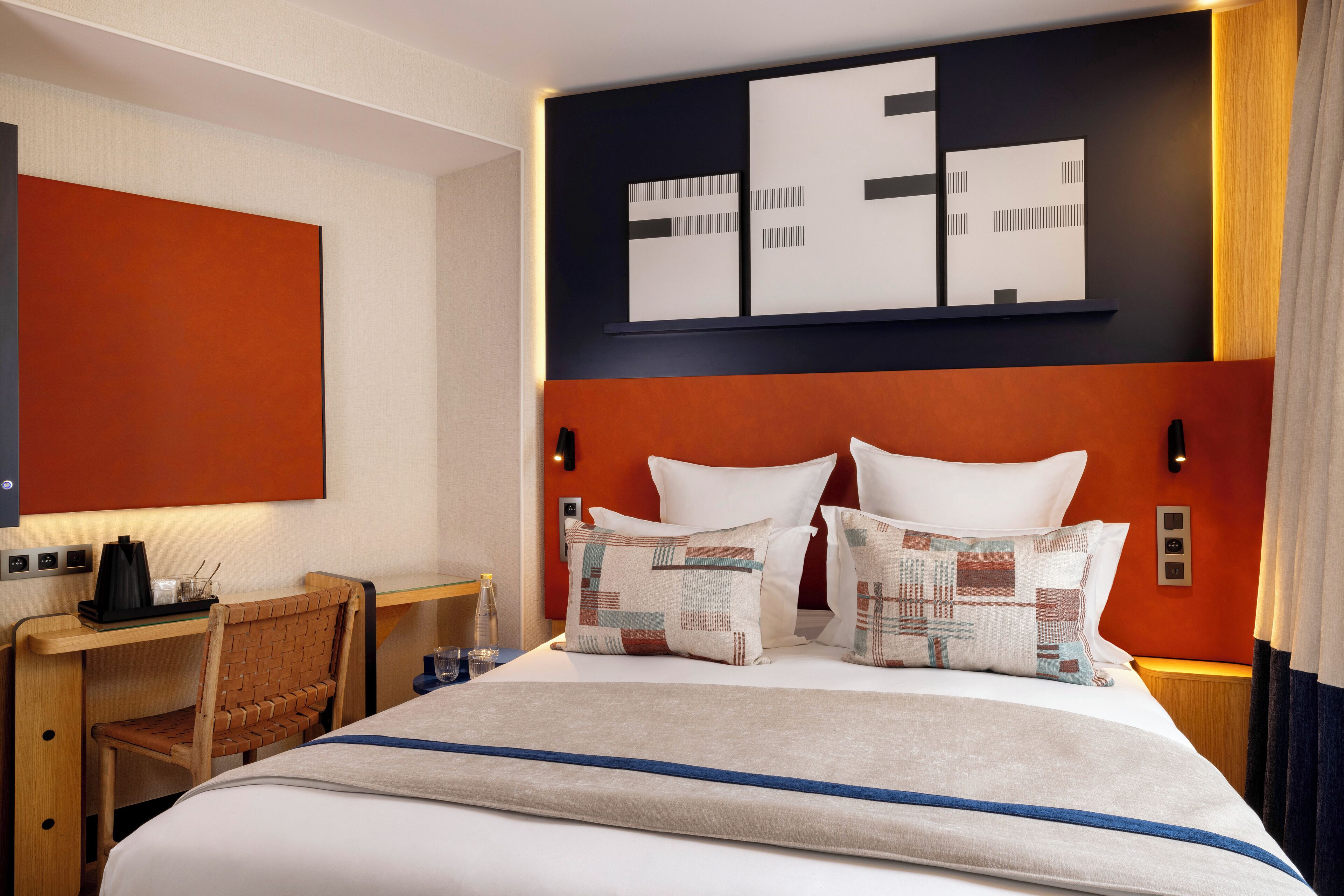 A hotel room with a large bed, a desk with a chair, and a wall-mounted artwork.
