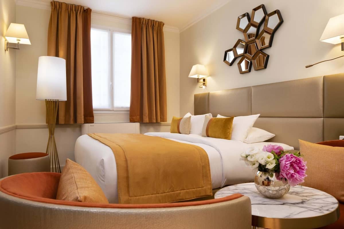 A hotel room with a large bed, two bedside tables, a round coffee table, and a decorative wall piece.