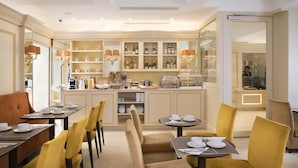 A hotel dining area with tables set for breakfast, yellow chairs, and a bar area with shelves of bottles.