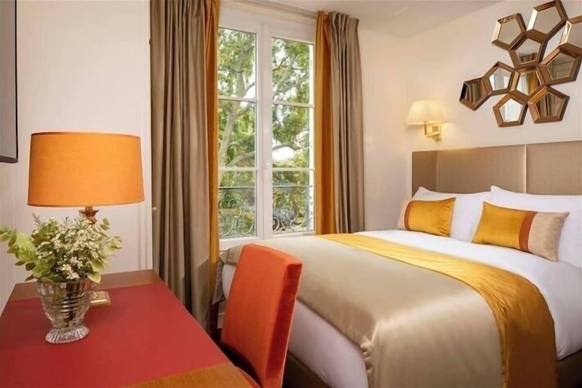 A hotel room with a bed, a table with a lamp, and a window with curtains.