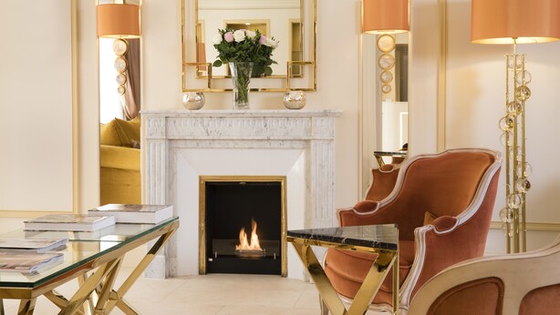 A room with a fireplace, a glass table, a red armchair, and a mirror with a gold frame.