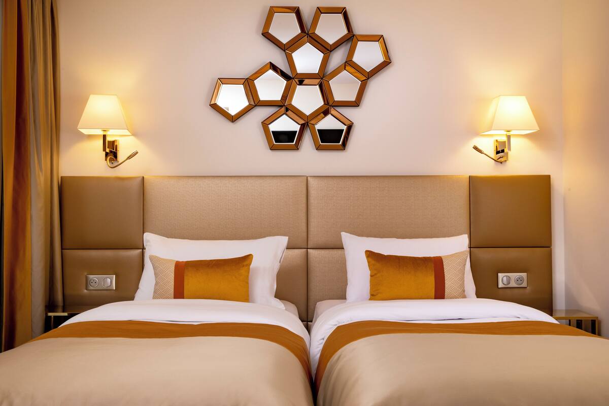 A hotel room with two beds, a geometric wall decoration, and bedside lamps.