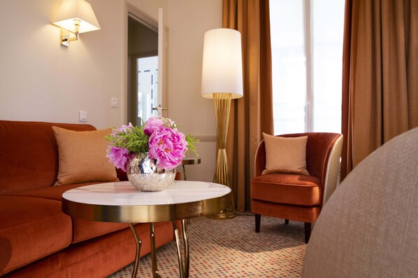 Habitación de hotel moderna con un sofá rojo, una mesa redonda con un jarrón de flores, una lámpara y vistas al exterior.