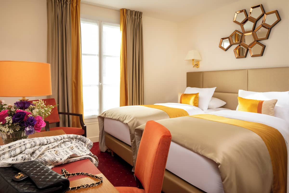 A hotel room with two beds, a desk with a lamp, a chair, and a decorative wall piece.