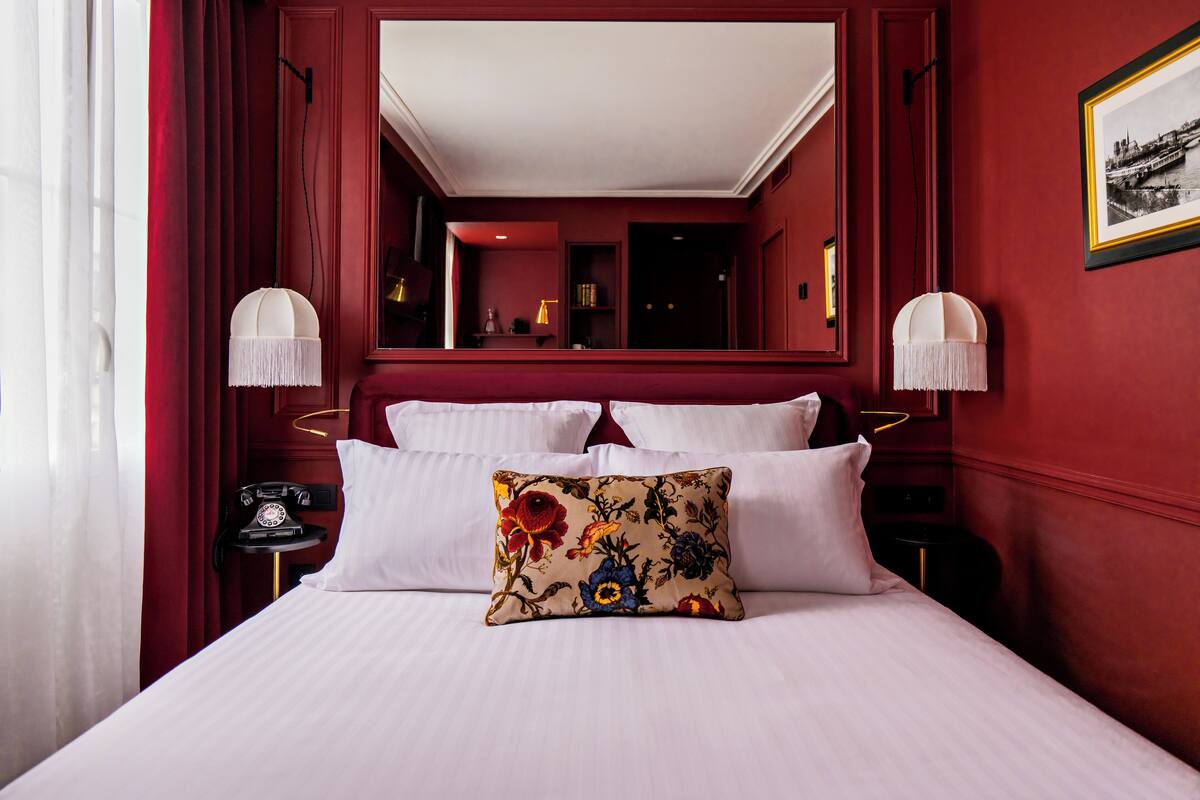 A hotel room with a large bed, white linens, a floral pillow, a telephone on the nightstand, and a framed picture on the wall.