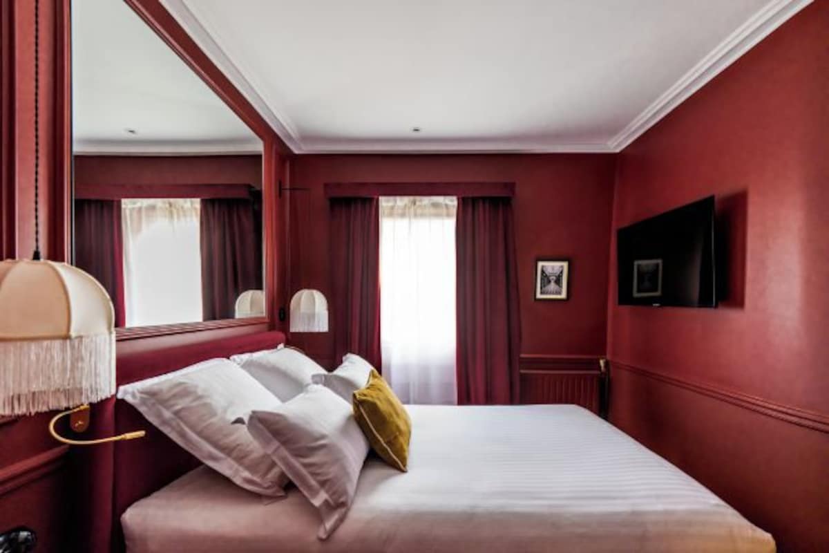 A hotel room with a large bed, a television mounted on the wall, and a window with curtains.