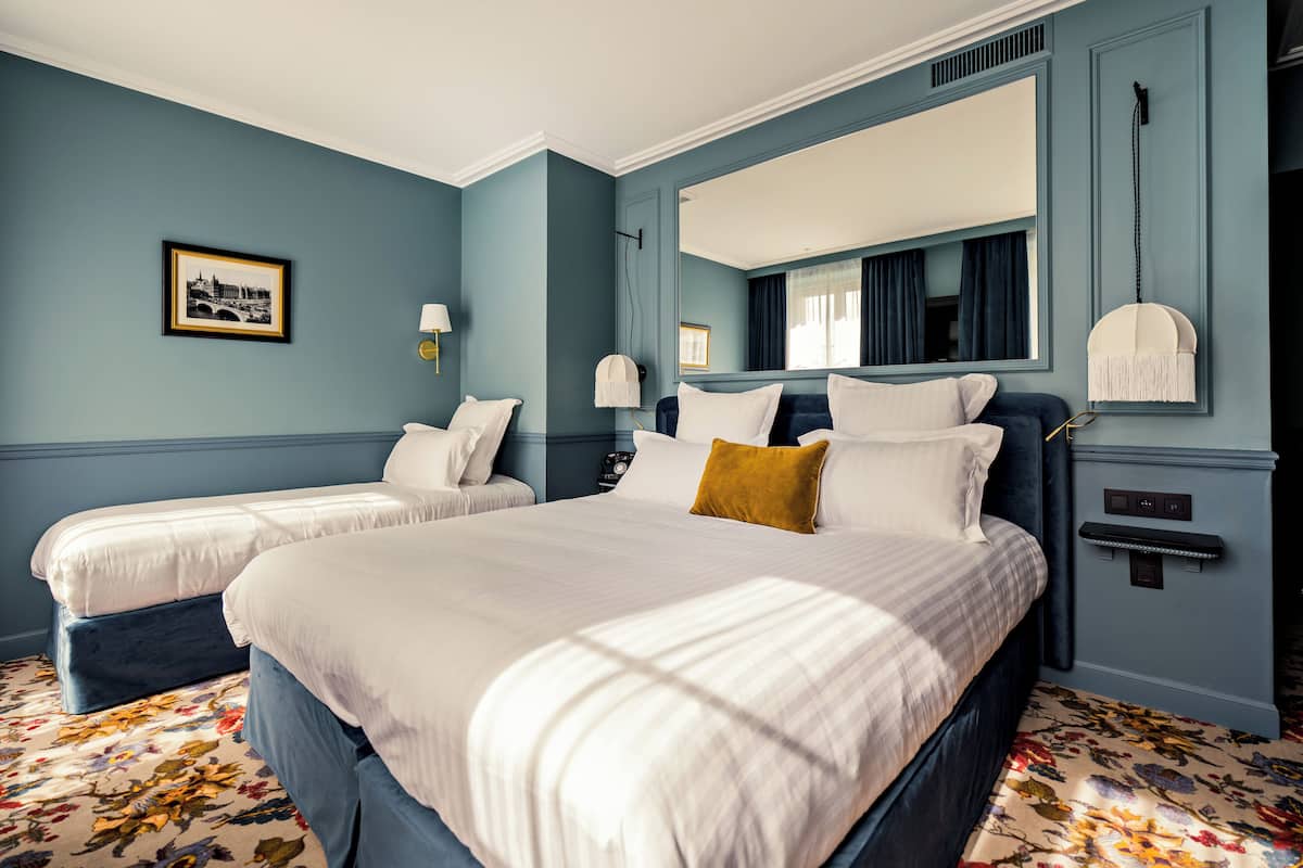 A hotel room with two beds, a large mirror, and a floral carpet.