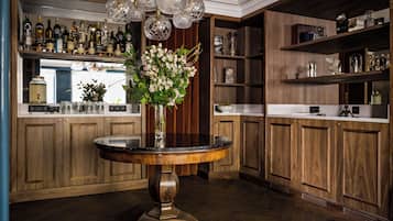 Eine Bar mit Holzsäulen, ein runder Tisch mit Blumen in einer Vase und hängende Kristallleuchten.
