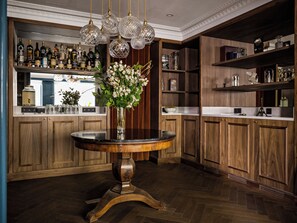 A bar area with wooden cabinets, a round table with a vase of flowers, and hanging crystal light fixtures.