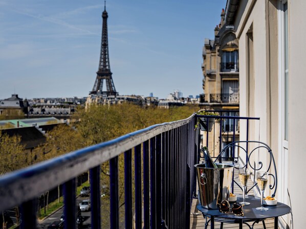 A balcony with a view of the Eiffel Tower, a metal table with a bottle, glasses, and a bowl of snacks.