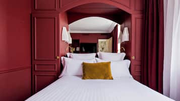 Une chambre avec un grand lit, du linge de lit blanc, un coussin de couleur moutarde et un mur rouge.