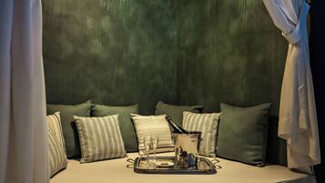 Un lit avec un plateau rempli de coupes à champagne et une bouteille, entouré d’oreillers à motifs.