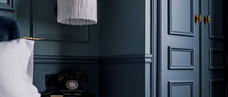 A room with a bed, a nightstand with a rotary phone, a white lamp, and a blue door.