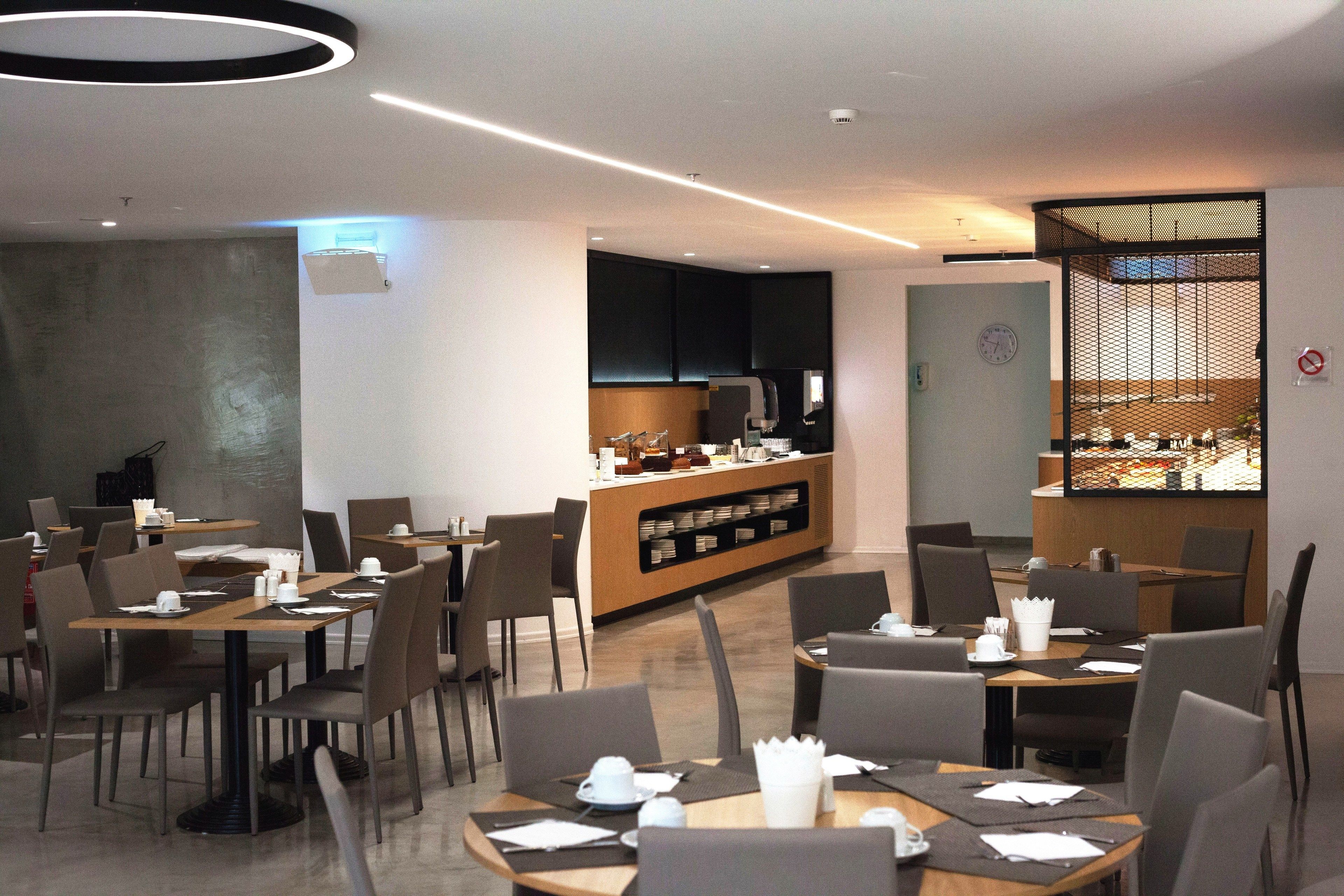 A modern restaurant with multiple tables and chairs, a counter with a display case, and a wall-mounted clock.