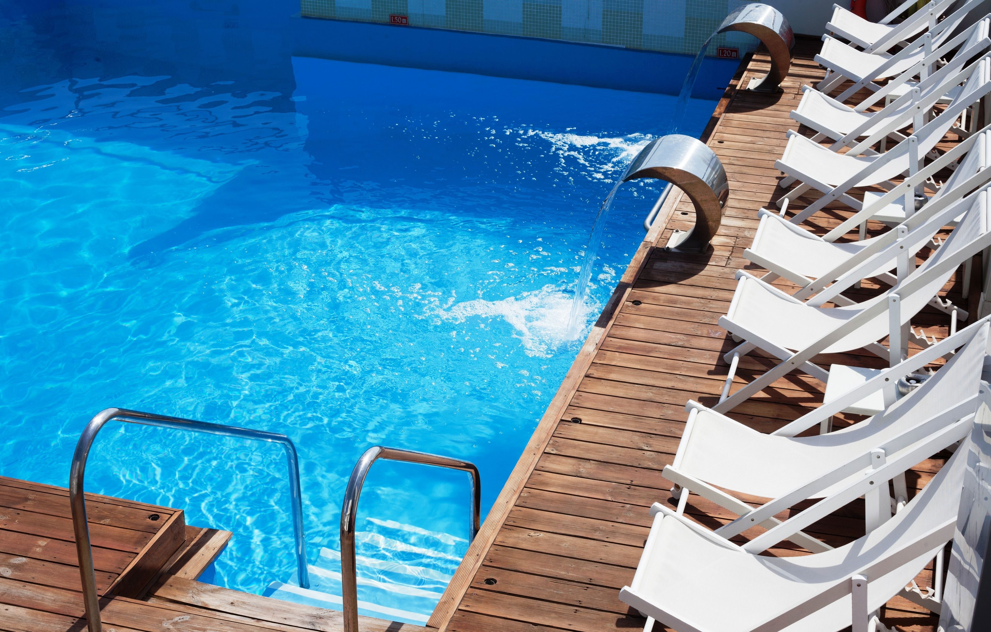 A swimming pool with a wooden deck and white lounge chairs.