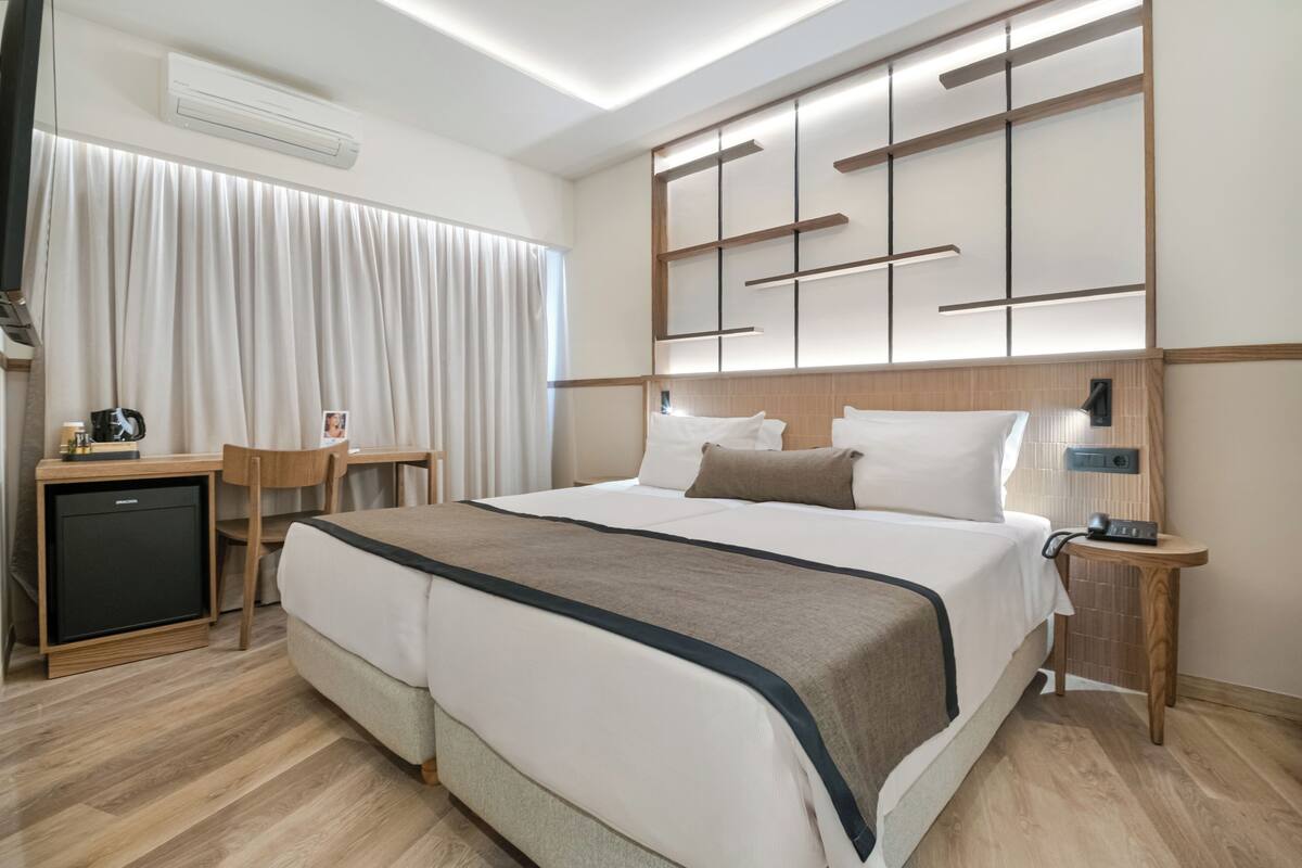 Ein modernes Hotelzimmer mit einem großen Bett, Nachttischen, einem Schreibtisch und einem kleinen Kühlschrank.