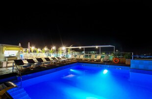 Un área de piscina nocturna con sillones de descanso y una zona de estar cubierta.