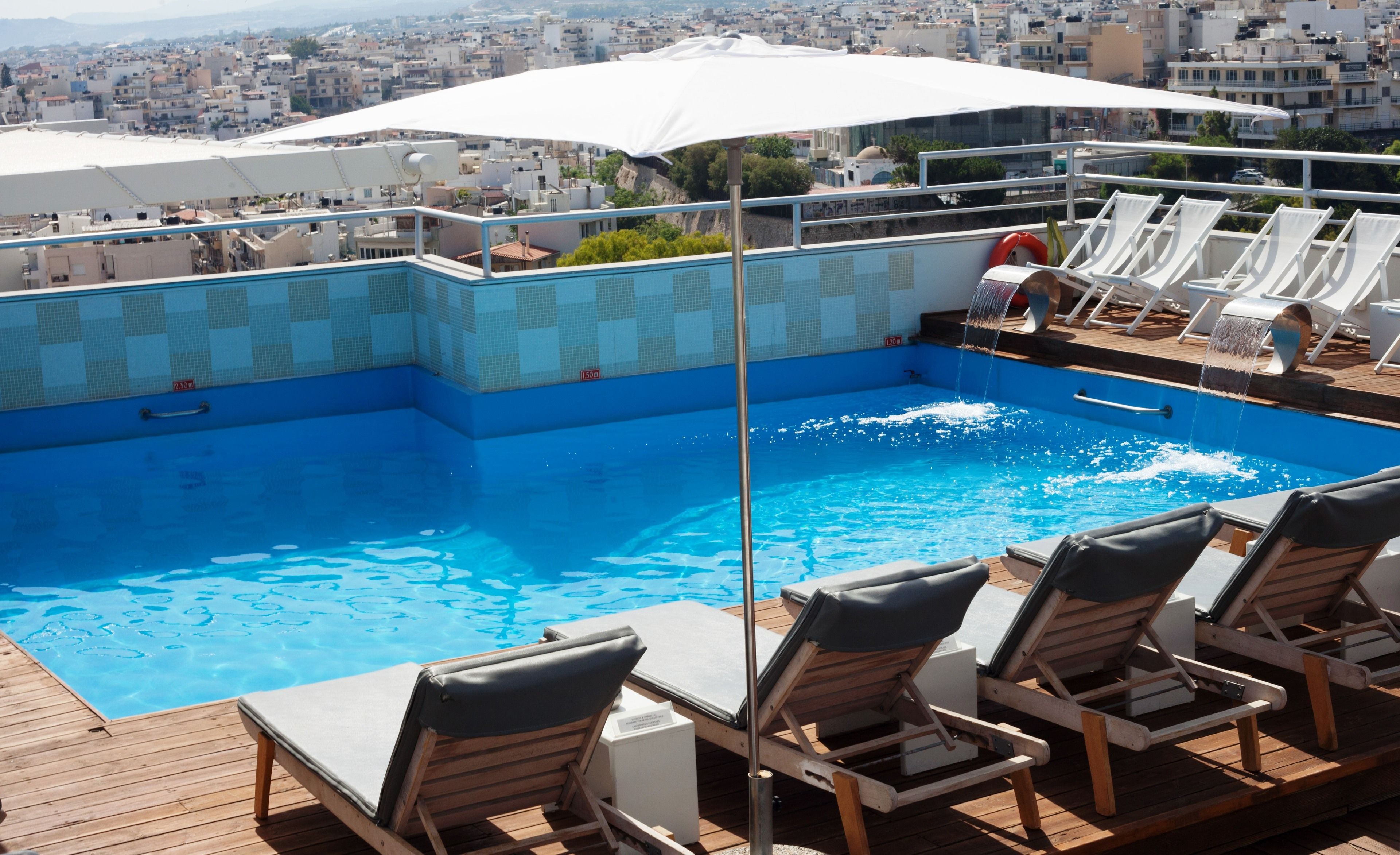 A rooftop pool with clear blue water, surrounded by wooden deck and lounge chairs.