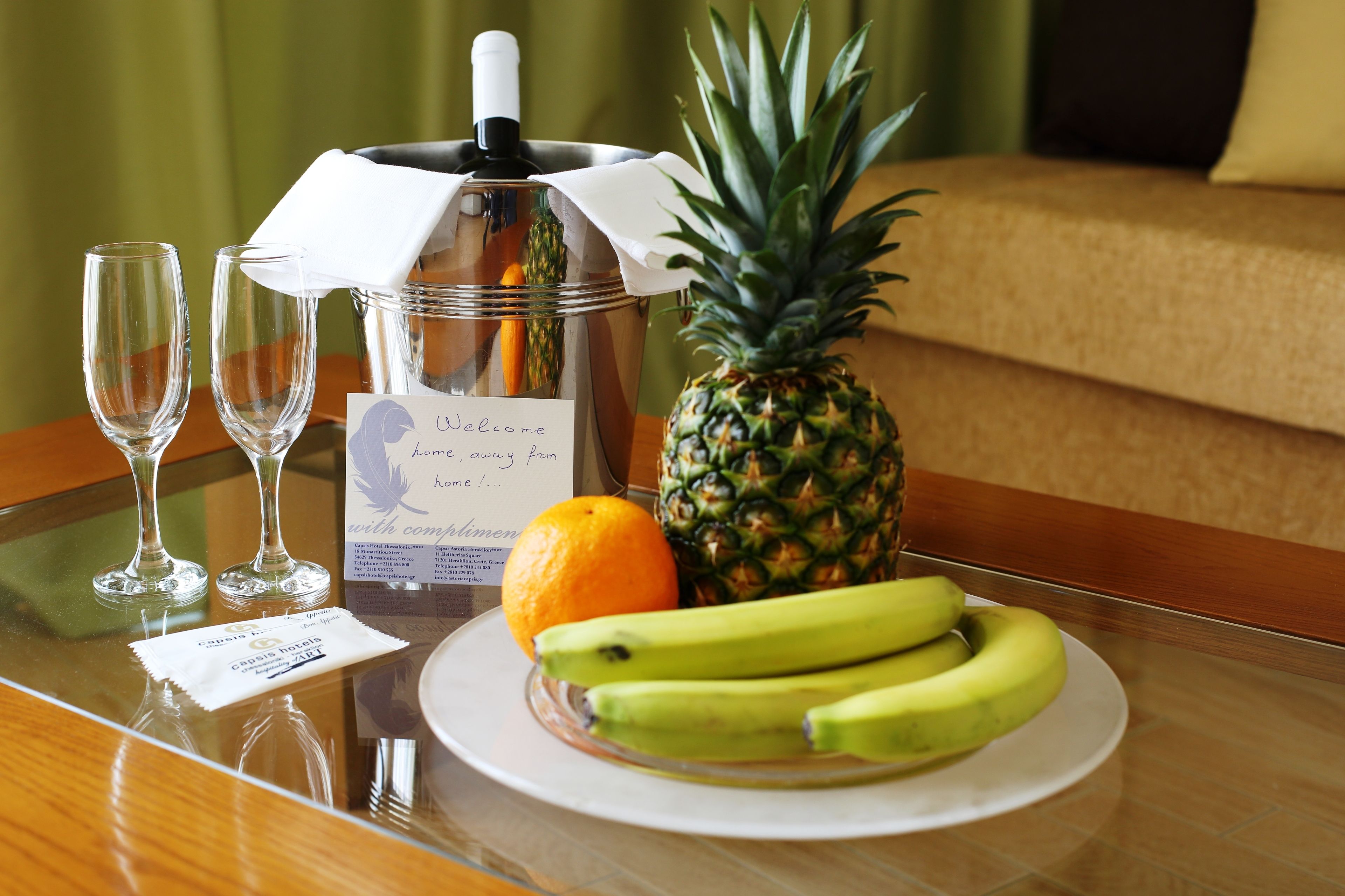 A table with a coffee pot, two wine glasses, a pineapple, bananas, an orange, and a menu.