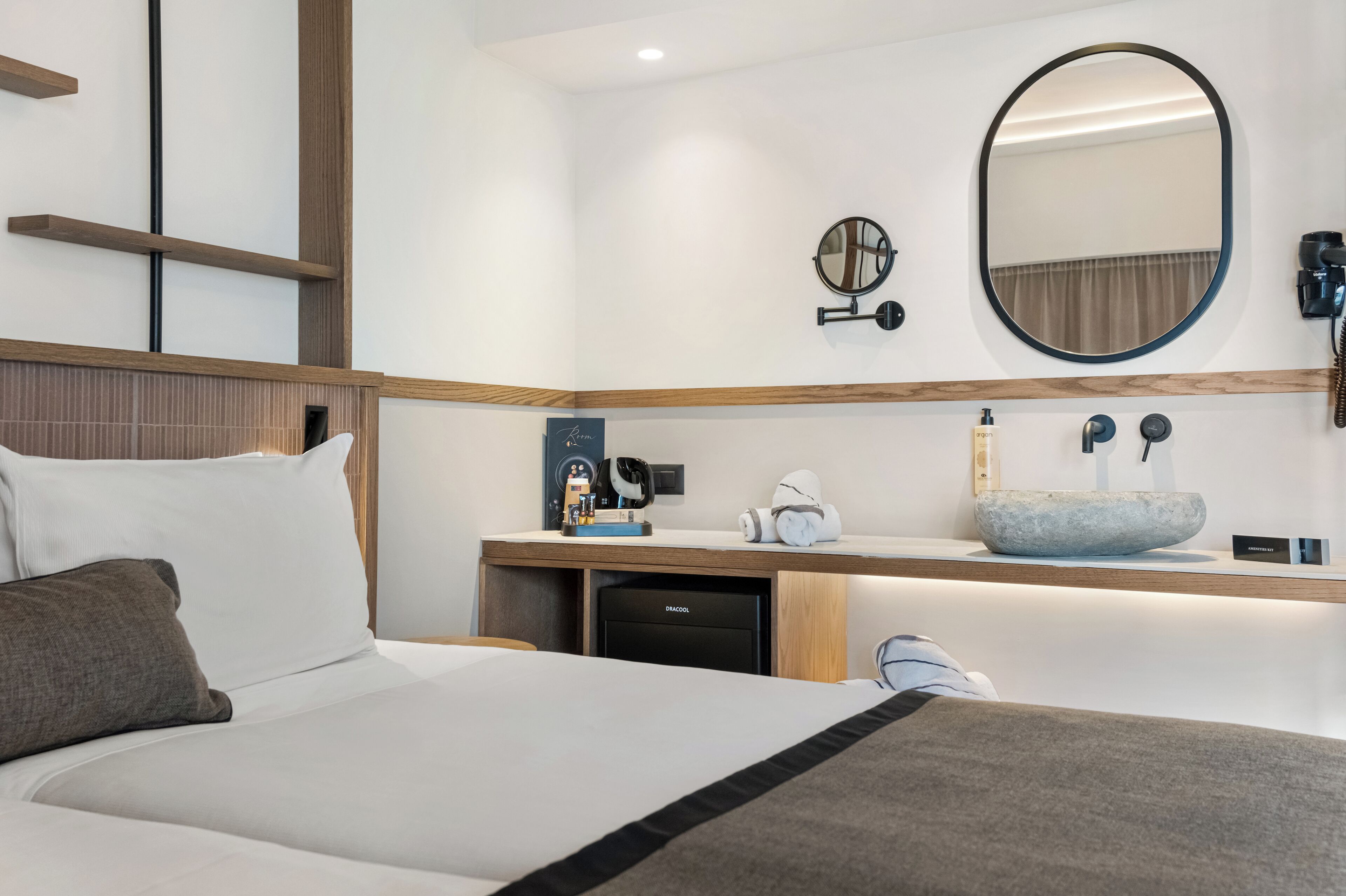 A hotel room with a bed, a desk with a sink, a mirror, and a small coffee machine.
