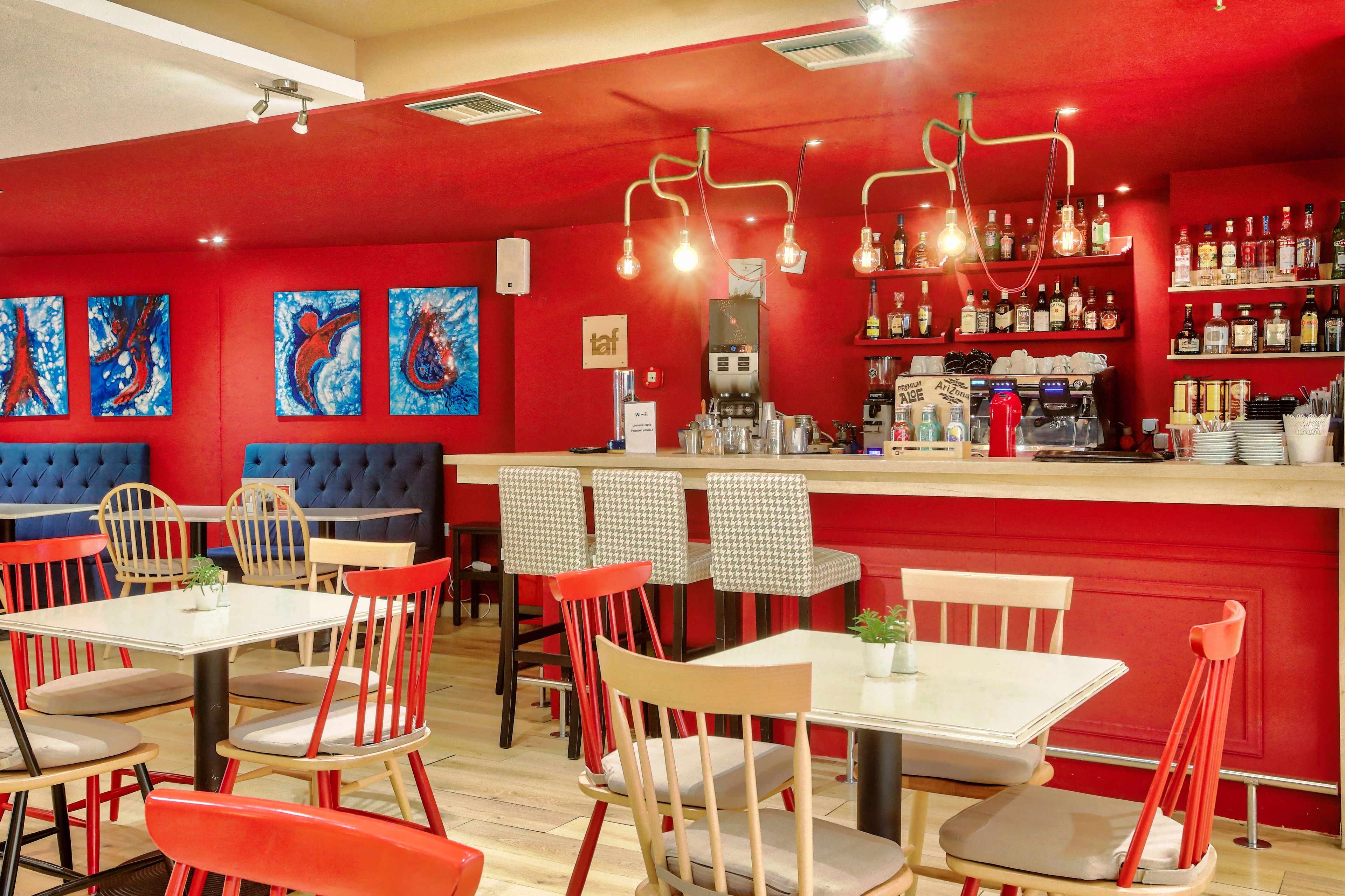Ein Restaurantinneres mit roten Wänden, mehreren Sitzbereichen und einer Bar mit verschiedenen Flaschen.