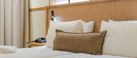 A neatly made bed with white linens and a brown pillow, a bedside telephone, and a wooden nightstand.
