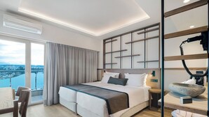 A modern hotel room with a large bed, a view of the city, and a balcony. - Capsis Astoria Heraklion Hotel (Heraklion)