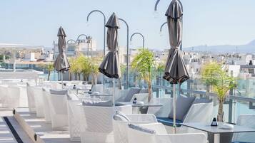 Une terrasse sur le toit, dotée de sièges extérieurs et de parasols, offrant une vue sur le paysage urbain.