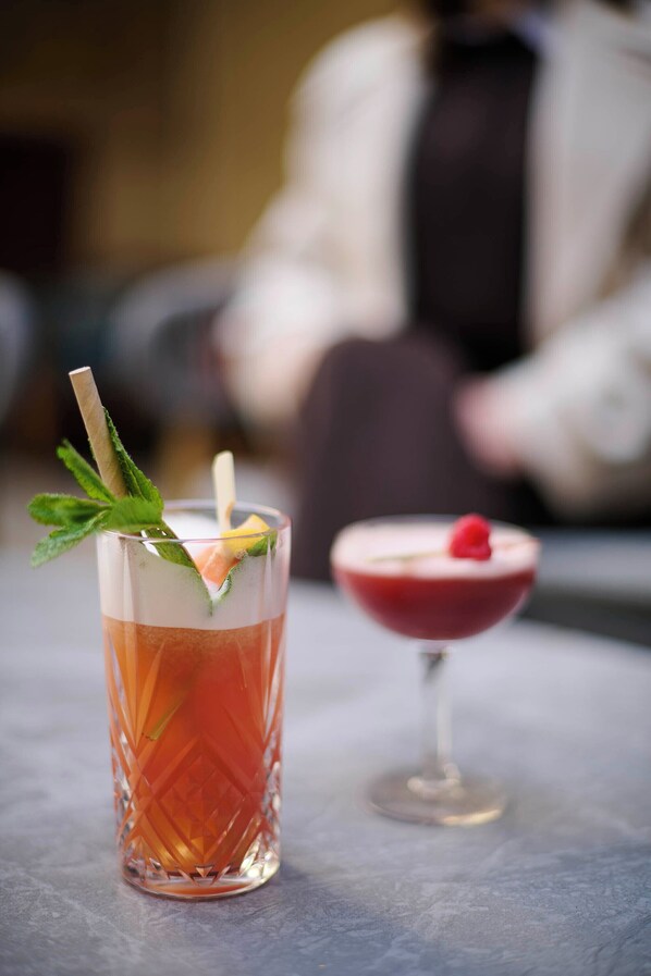 A cocktail glass with a mint garnish and a cocktail in a glass with a red rim and a raspberry on top.