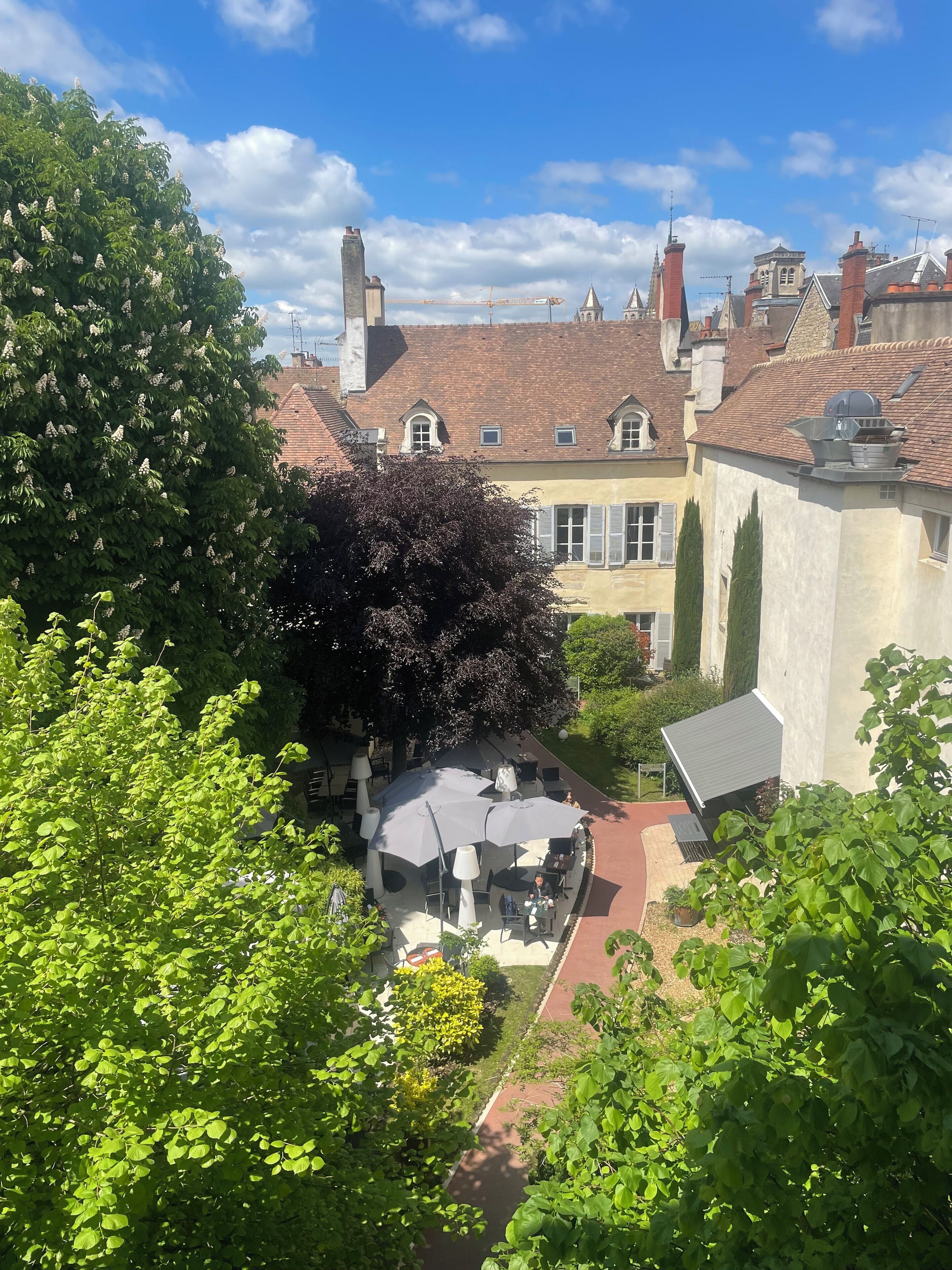 Une cour intérieure dotée d’un espace pour s’asseoir, entourée d’arbres et de bâtiments aux toits recouverts de tuiles rouges.