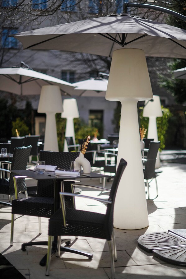 Outdoor tables with chairs, umbrellas, and a white vase with flowers.