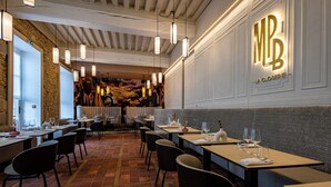 A restaurant interior with a tiled floor, multiple dining tables, chairs, and hanging pendant lights. - Hôtel Philippe le Bon (Dijon)