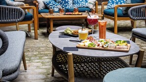 An outdoor seating area with wooden furniture and a stone floor, featuring a table with food and drinks. - Hôtel Philippe le Bon (Dijon)