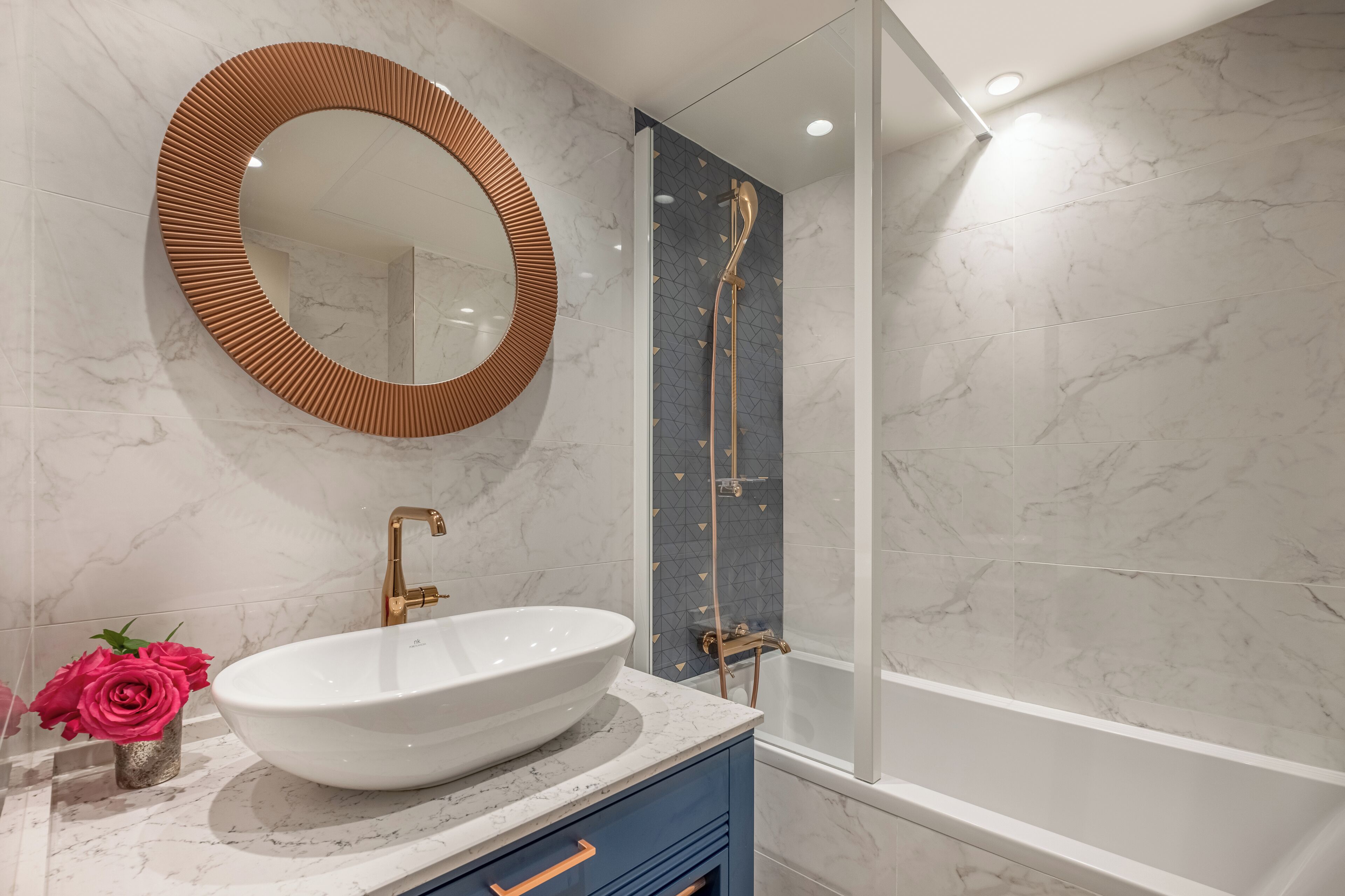 A bathroom with a white sink, a round mirror, and a shower with a gold showerhead.