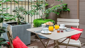 Un pequeño espacio al aire libre con zona de comedor y mesa dispuesta para el desayuno, con croissants, zumo de naranja y té.