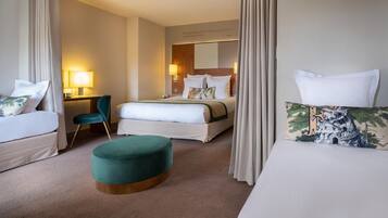A hotel room with two beds, a desk, a chair, and a small ottoman.
