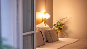 Un dormitorio con cama, almohadas, una lámpara de noche y un florero con flores.