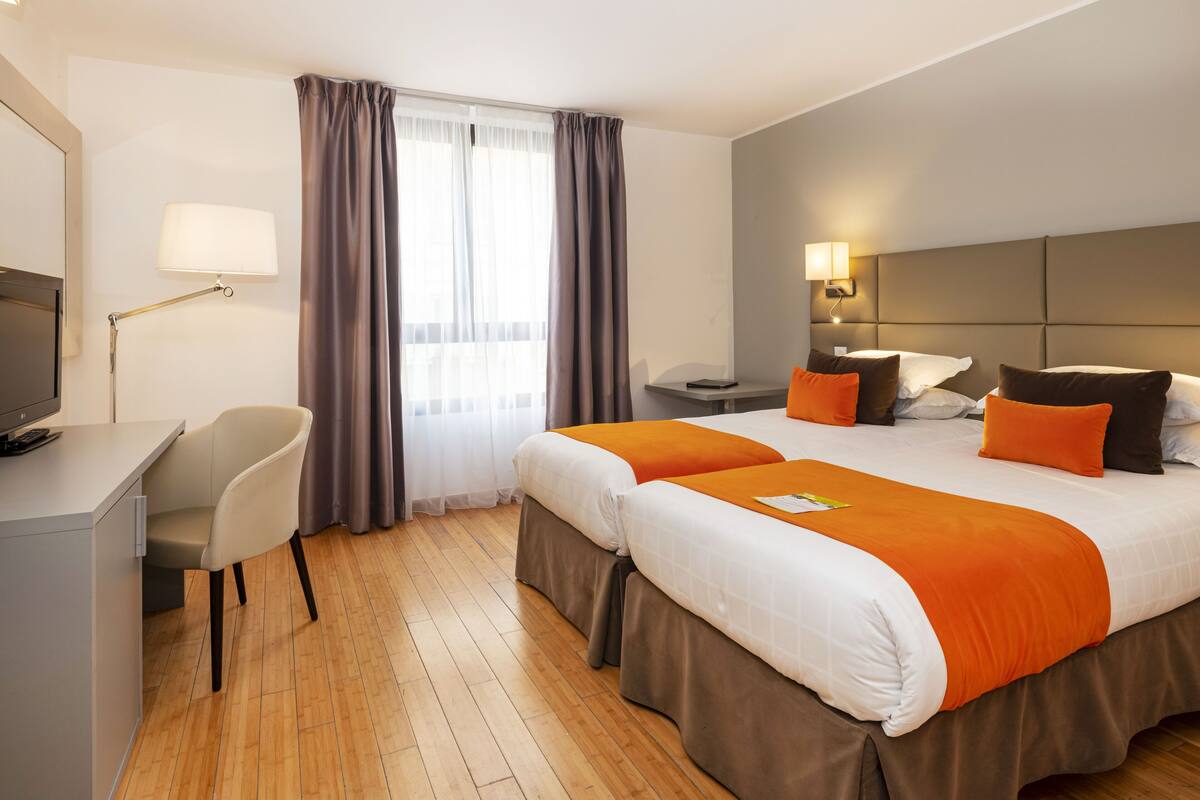 A hotel room with a bed, a desk, a chair, a TV, and a window with curtains.