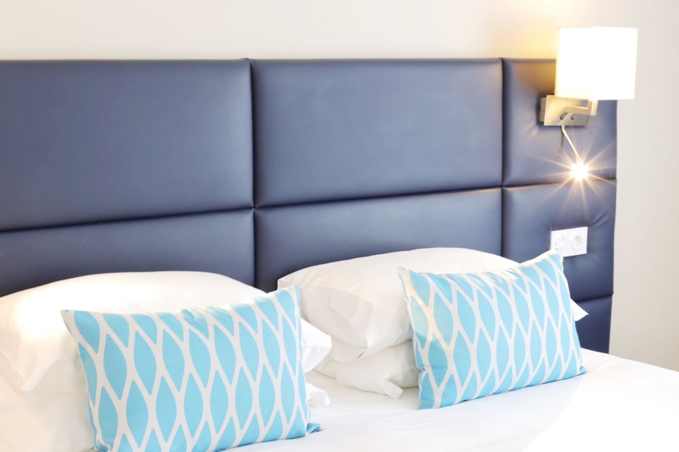 Camera d'albergo con una testiera scura, biancheria da letto bianca e cuscini decorati.
