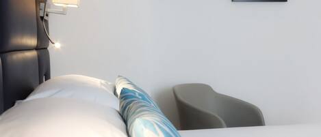 Hotelkamer met een bed, nachtkastje met een lamp, een lijst aan de muur en een stoel.