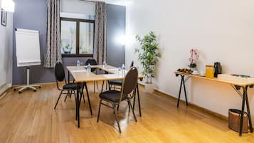 Un salón de conferencias con una pizarra, una mesa con sillas, una planta en maceta y un espacio para café.