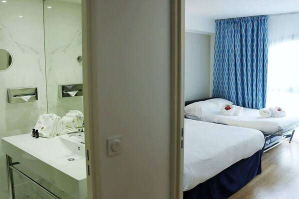 Una habitación de hotel con baño, cama y ventana con cortinas.