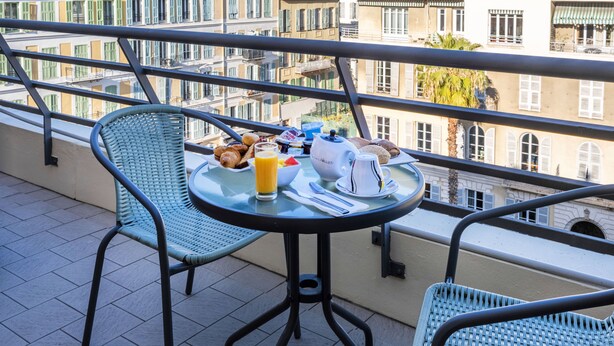 A balcony with a table set for breakfast, including croissants, juice, and a teapot. - Hotel Nice Riviera (Nice)