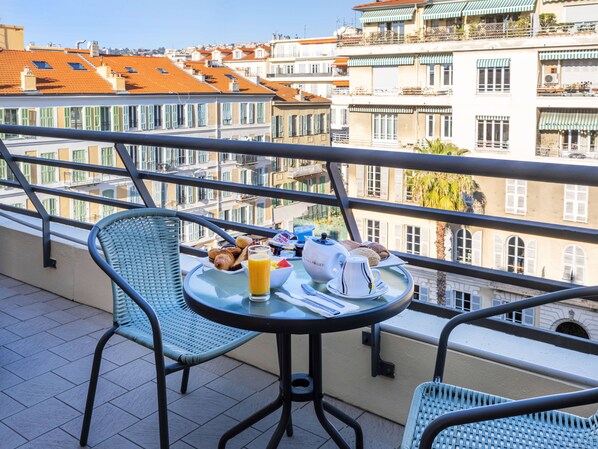 Un balcón con una mesa dispuesta para el desayuno, que incluye croissants, jugo y una tetera.