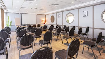 A conference room with rows of chairs, a projector screen, and a table with a lamp.
