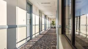 A hotel corridor with a stone-tiled floor, doors numbered 604, and a potted plant in the distance. - Hotel Nice Riviera (Nice)
