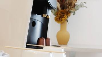 A modern coffee machine with a sleek black design, a white countertop, and a vase with dried flowers in the background.