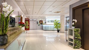 A modern hotel lobby with a marble floor, a reception desk, and potted plants. - Hotel Nice Riviera (Nice)