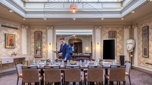 A formal dining room with a high ceiling and skylight, a long table set for a meal, and a waiter serving. - Hôtel Littéraire le Swann, BW Premier Collection (Paris)