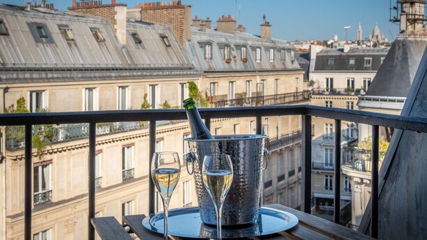 A balcony with a table set for two, featuring a champagne bottle and glasses, overlooking a cityscape with historic buildings. - Hôtel Littéraire le Swann, BW Premier Collection (Paris)